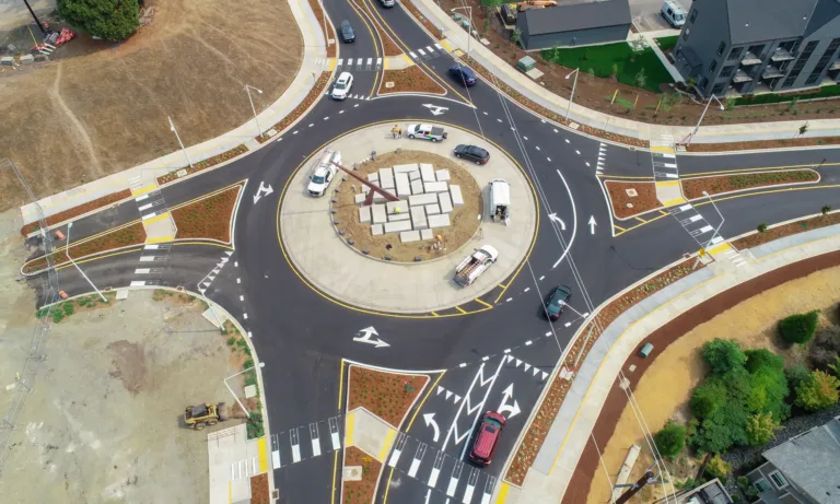 Aerial view of a newly constructed multilane roundabout in a suburban neighborhood, with cars navigating clearly marked lanes around a landscaped central island and splitter islands.