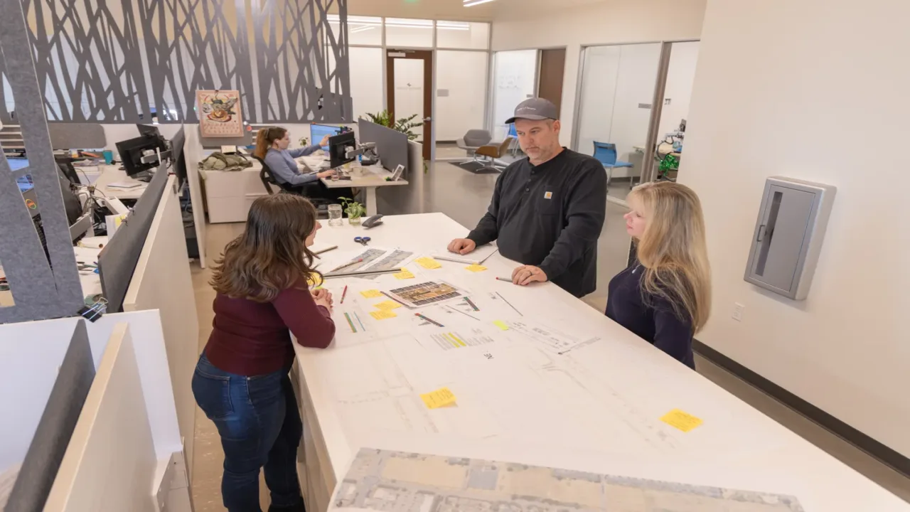 MacKay Sposito team collaborating over civil engineering site plans with sticky notes at a standing table in a modern open office.
