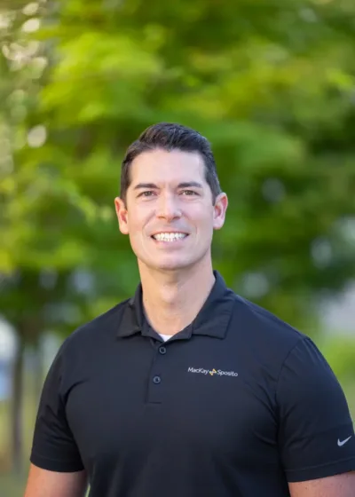 Headshot of Jason Joyce smiling in a black polo with the MacKay Sposito logo, outdoors against a blurred green background.