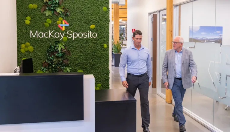 MacKay Sposito office lobby featuring a green living wall and logo, with two team members walking past the reception.