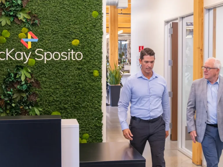 MacKay Sposito office lobby featuring a living green wall with the company logo, as two team members walk through a modern hallway with glass-walled offices and wood beams.