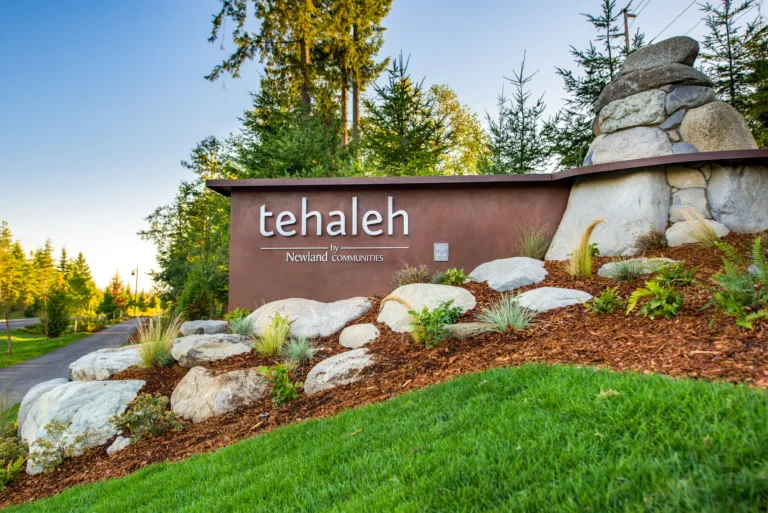 Entrance monument sign reading “tehaleh by Newland Communities,” surrounded by landscaped rocks and greenery with evergreen trees in the background.