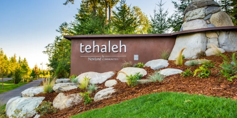 Entrance monument sign reading “tehaleh by Newland Communities,” surrounded by landscaped rocks and greenery with evergreen trees in the background.